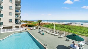 Ein Poolbereich mit Liegestühlen und Sonnenschirmen mit Blick auf einen Strand und das Meer.