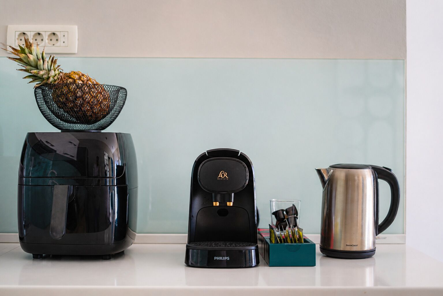 Una encimera de cocina con cafetera, hervidor y frutero.
