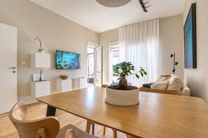 A modern living room with a wooden dining table, a potted plant, a flat-screen TV, and a sofa. - Deluxe beach suite with hot tub, 2 minutes away from the beach (Split)
