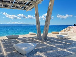 A beach with a concrete structure, seating areas, and a view of the sea. - Deluxe beach suite with hot tub, 2 minutes away from the beach (Split)
