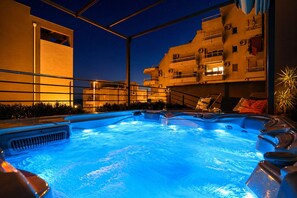 A swimming pool with hot tubs, surrounded by a metal fence, and adjacent to a building with balconies.
