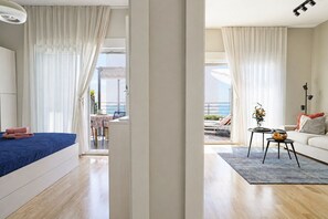 A modern hotel room with a bed, a dining area with a table and chairs, a sofa, and a view of the outdoors.