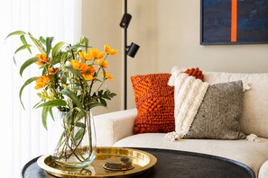 A living room with a sofa, a vase with flowers, a lamp, and a painting on the wall.