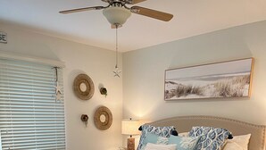 A bedroom with a bed, wooden flooring, a ceiling fan, a nightstand, and a wall-mounted lamp. - Bethany Beach • Lakefront Sea Colony Condo • Walk to Beach • Sleeps 8 (Bethany Beach)
