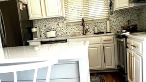 A modern kitchen with white cabinetry, a large island with a white chair, and a wooden floor. - Bethany Beach • Lakefront Sea Colony Condo • Walk to Beach • Sleeps 8 (Bethany Beach)