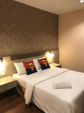 A hotel room with a patterned wallpaper, a bed with white bedding, two Superman-themed pillows, and bedside lamps. - Victory Hotel (Johor Bahru)