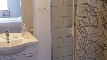 Un baño con lavamanos blanco, espejo y ducha con cortina de motivos florales.
