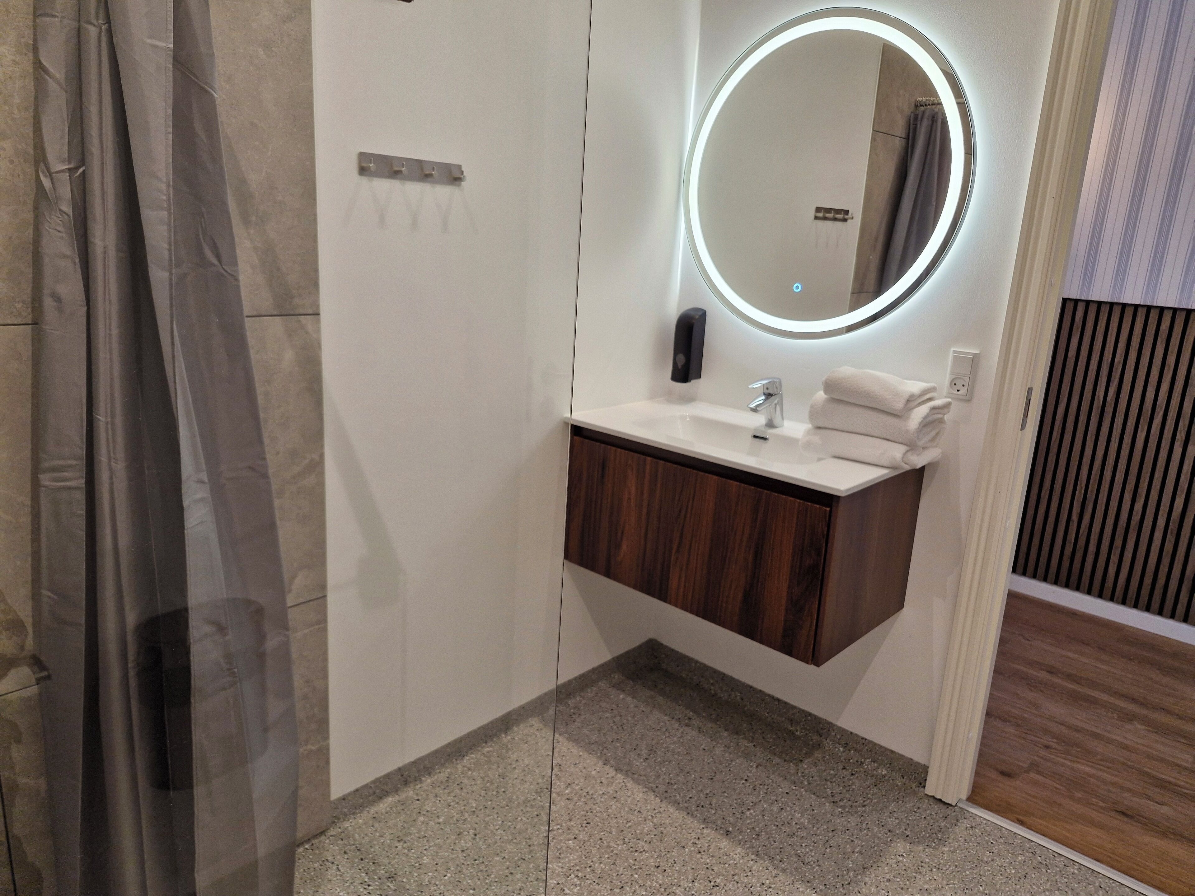 A bathroom with a white sink, a mirror with a circular light, a towel rack, and a shower curtain.