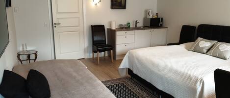 A bedroom with two beds, a desk, a chair, a small table, and a wall-mounted light.