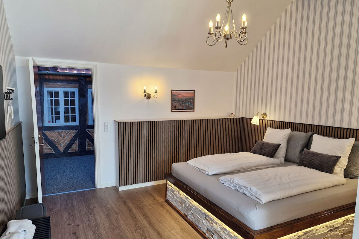 A bedroom with a wooden headboard, a large bed with white linens, a chandelier, and a view of the outside.