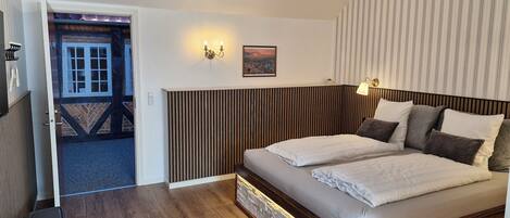 A bedroom with a wooden headboard, a large bed with white linens, a chandelier, and a view of the outside.