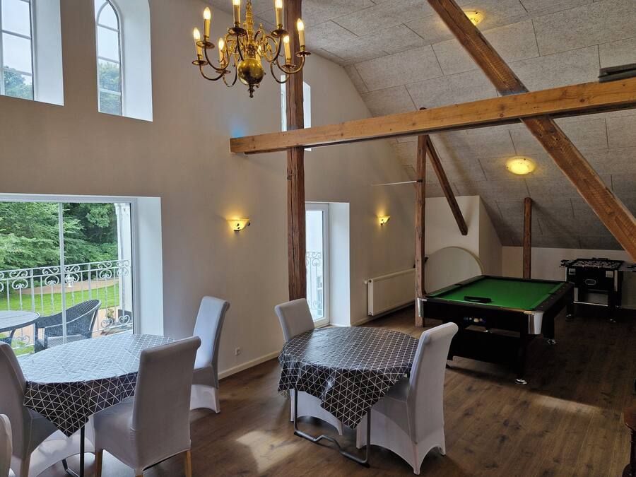 Een kamer met een biljarttafel, een eettafel met stoelen, een kroonluchter en uitzicht op het omliggende landschap.