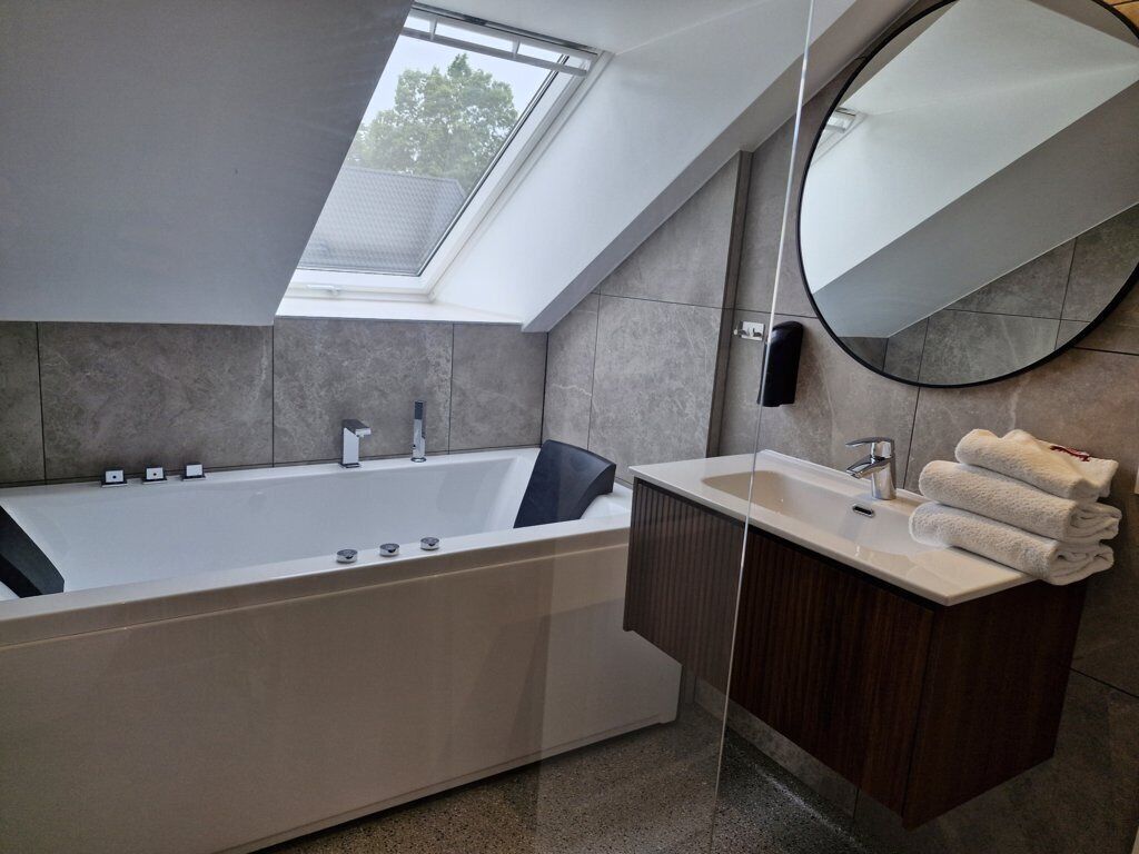 A modern bathroom with a freestanding bathtub, a vanity with a mirror, and a skylight above the tub.