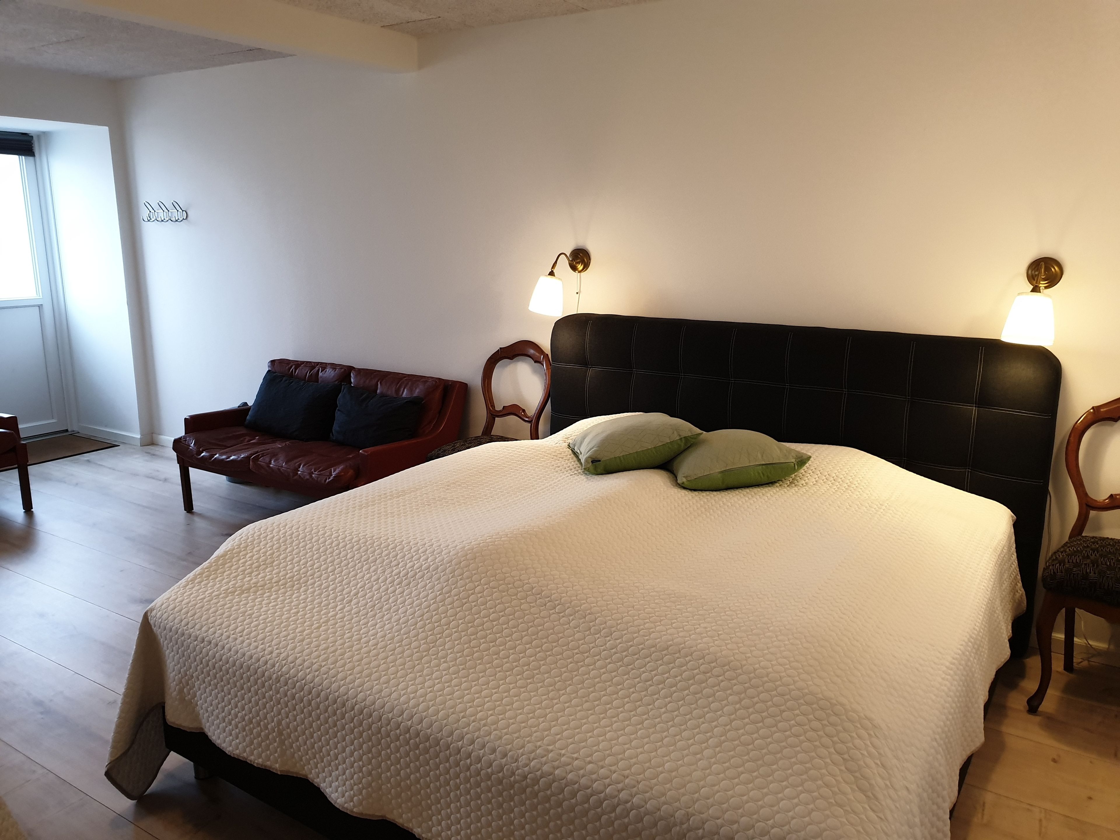 Habitación de hotel con una cama grande, dos lámparas fijadas a la pared, un sofá de cuero rojo y suelo de madera.