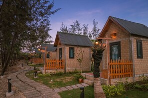 A row of small, rustic cabins with wooden exteriors and metal roofs, surrounded by a landscaped garden with a stone pathway. - Longhai Channel Beach Resort (Ho Chi Minh City)