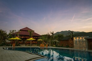 A swimming pool with lounge chairs and umbrellas, a restaurant with a red roof, and a stone wall with the text "LONG HAI CHANNEL". - Longhai Channel Beach Resort (Ho Chi Minh City)