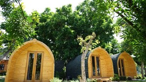 Two wooden arched cabins with large sliding doors, surrounded by lush greenery and trees.
