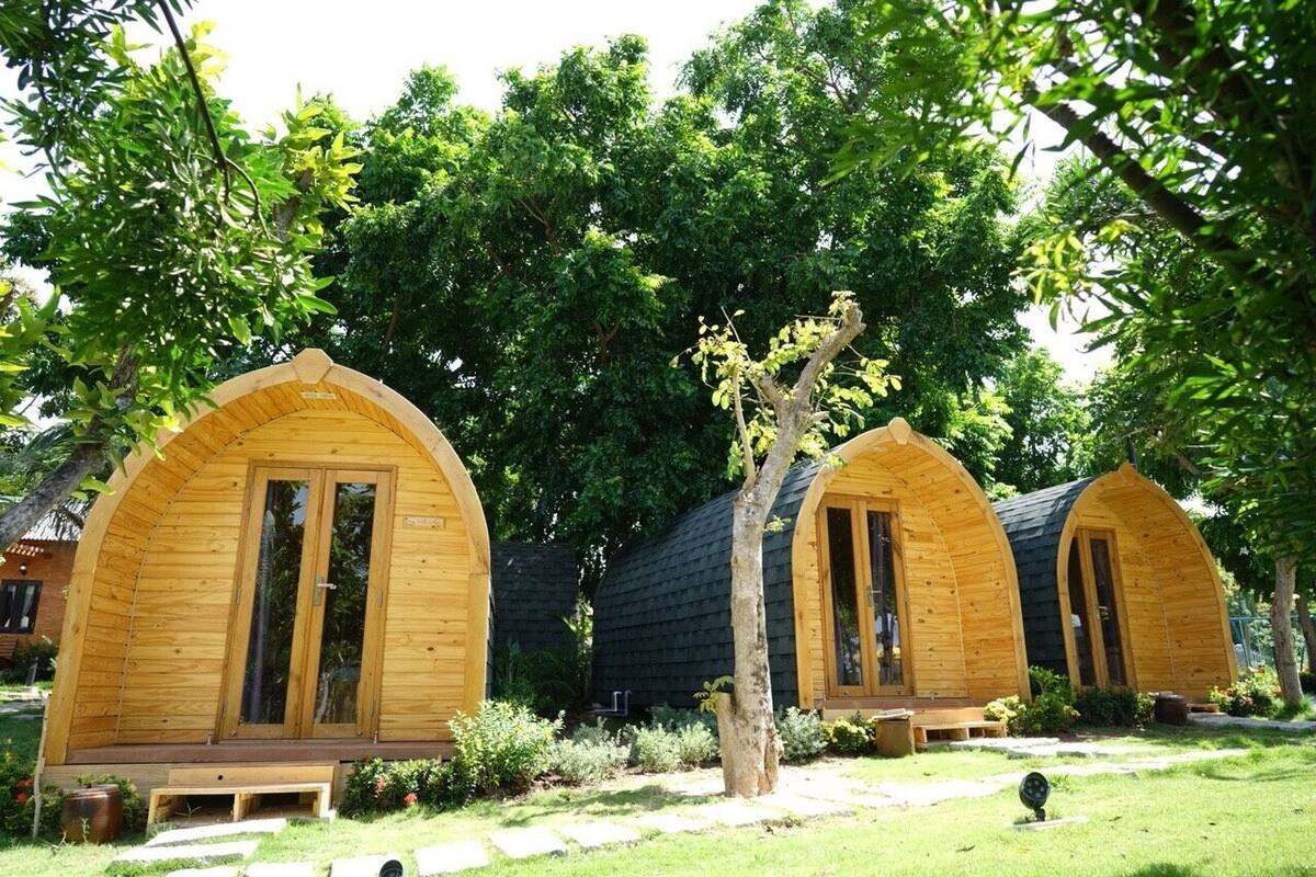 Two wooden arched cabins with large sliding doors, surrounded by lush greenery and trees.