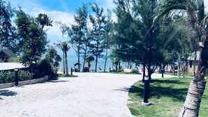 A paved walkway leading to a beach area with palm trees and a view of the ocean.
