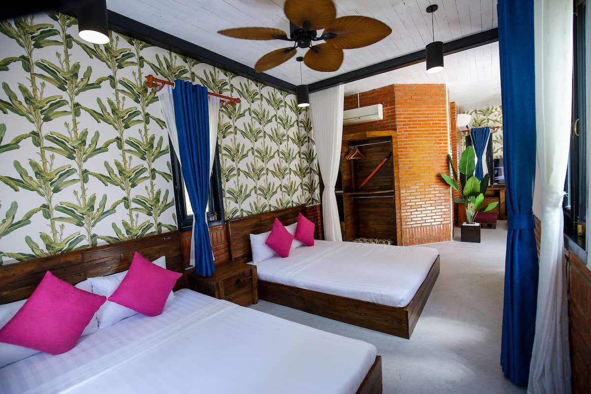 A hotel room with two beds, a ceiling fan, a brick wall, and a plant.