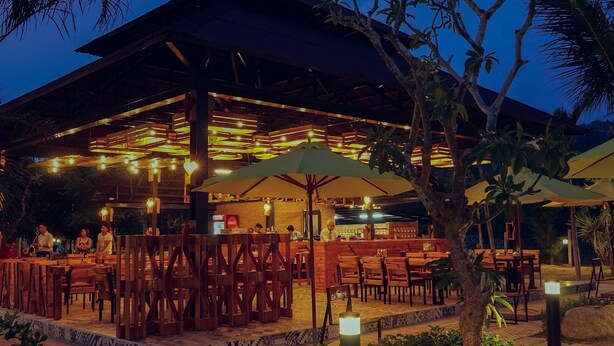 An outdoor restaurant with wooden tables and chairs, umbrellas, and string lights.