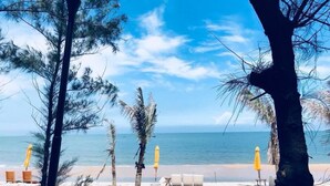 A beach with a lamp post, palm trees, and yellow umbrellas.