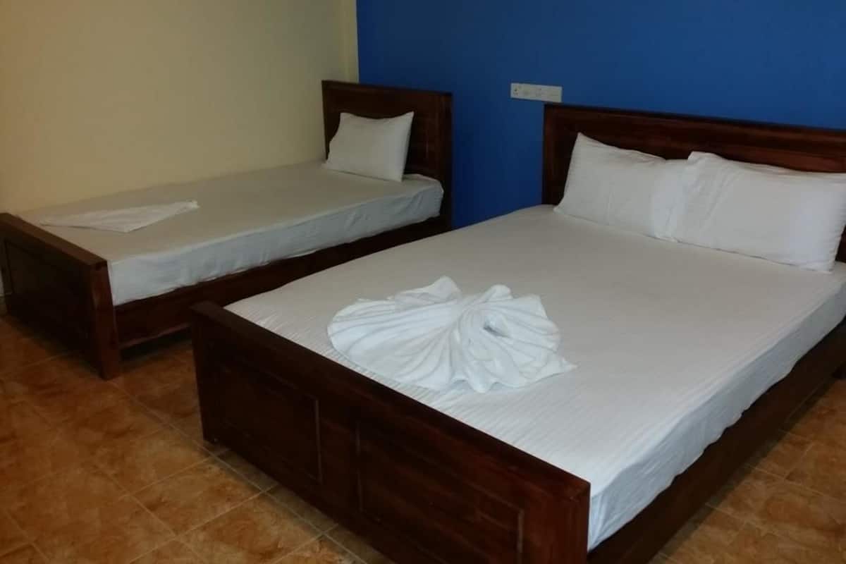 Deux lits simples avec des têtes de lit en bois et du linge de lit blanc, dans une chambre dont un mur est peint en bleu et dont le sol est carrelé.