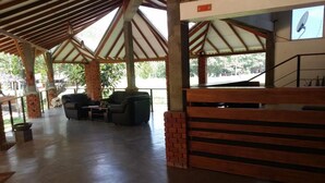 A covered outdoor seating area with brick pillars, a wooden bench, and a television screen. - Hotel Araliya (Kekirawa)