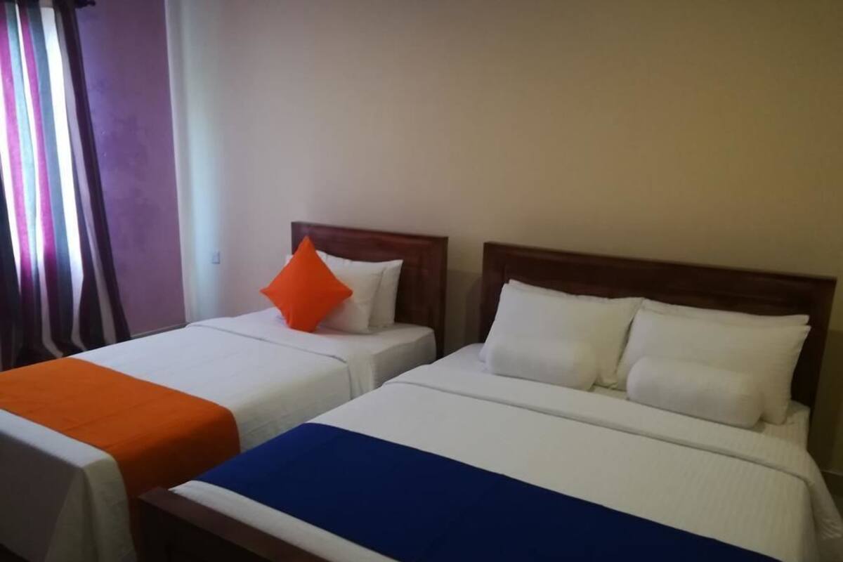 Deux lits simples avec des têtes de lit en bois, une literie blanche et un oreiller orange sur l’un des lits.