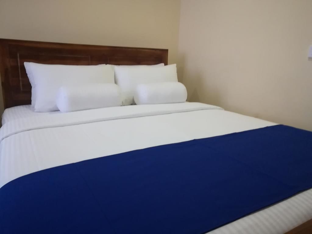 Una cama bien hecha con ropa de cama blanca y azul, un cabecero de madera y una pared lisa.