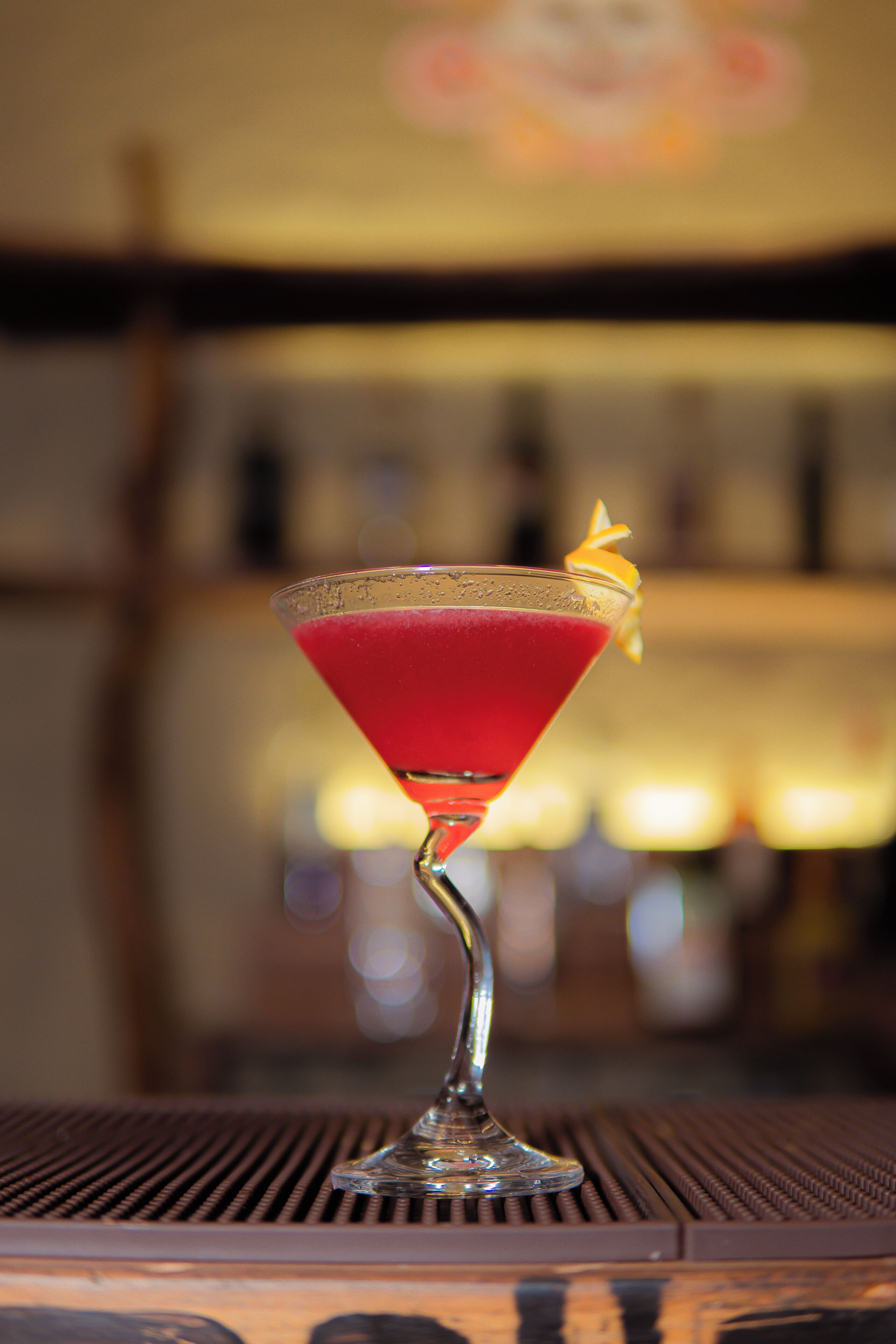 Una copa de martini con una bebida roja sobre una barra.