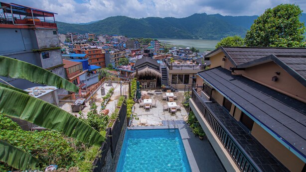 A residential area with a swimming pool, a thatched-roof structure, and a view of mountains and a lake. - Pokhara Boutique Hotel (Pokhara)