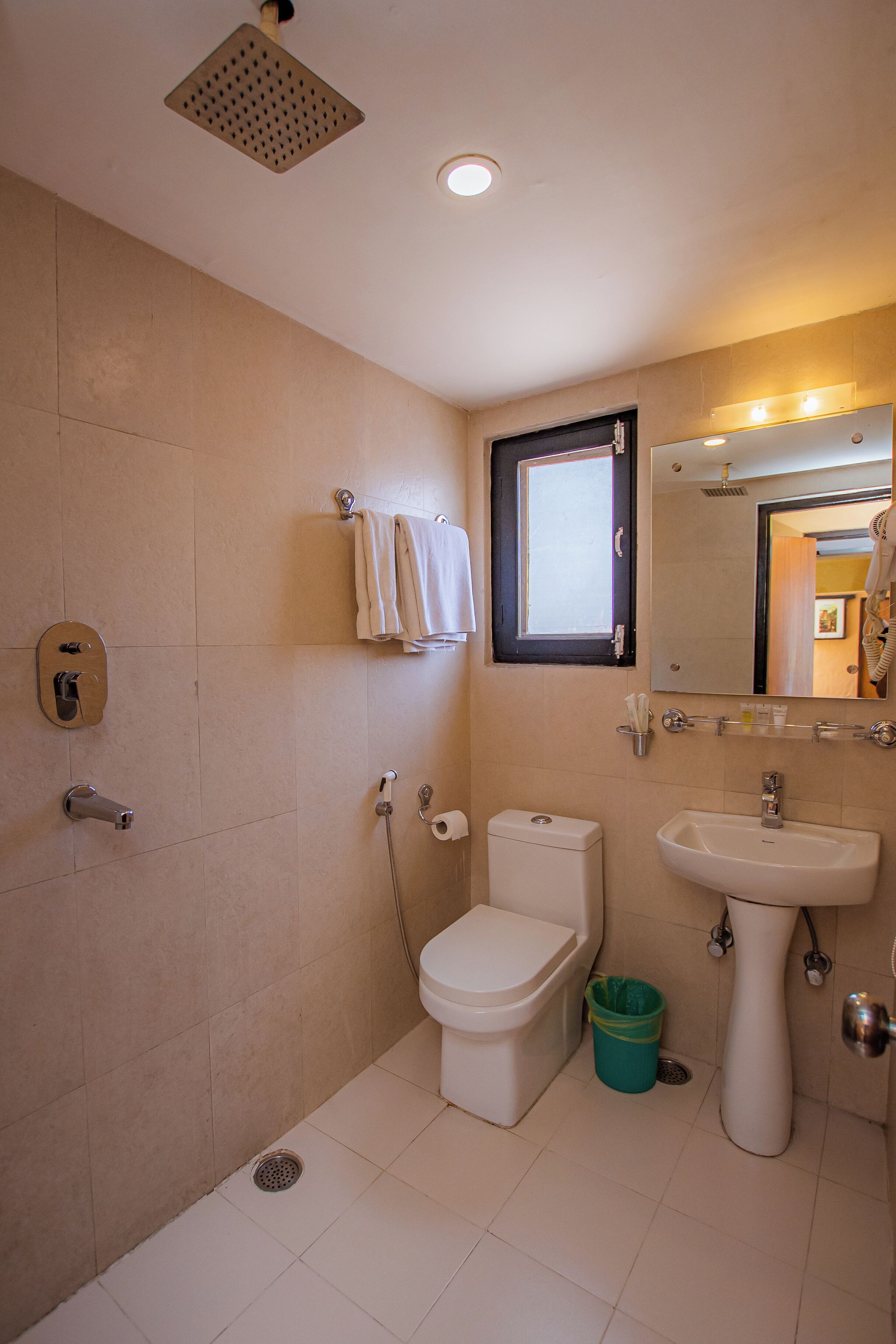 A bathroom with a toilet, sink, shower, and a window.