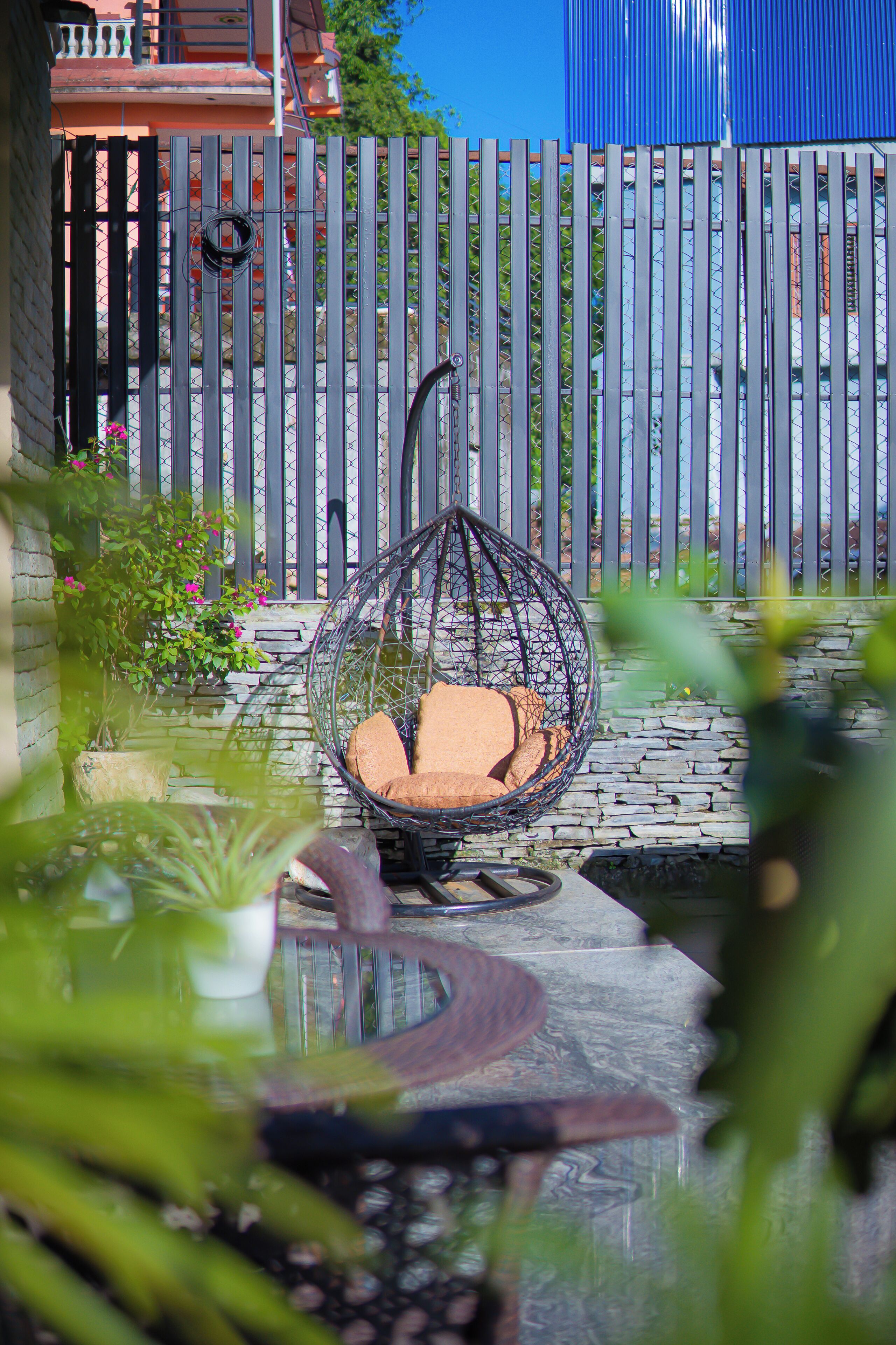 A wicker chair with cushions, a stone wall, and a metal fence in a garden setting.
