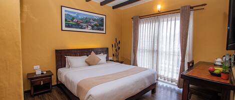 A hotel room with a wooden bed, a nightstand, a desk with a plant, and a painting on the wall.