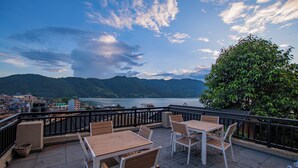 A terrace with tables and chairs overlooking a lake and mountains. - Pokhara Boutique Hotel (Pokhara)
