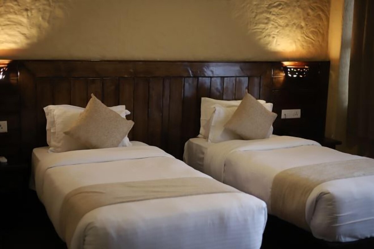 Una camera d'albergo con due letti singoli, ognuno con cuscino e coperta.