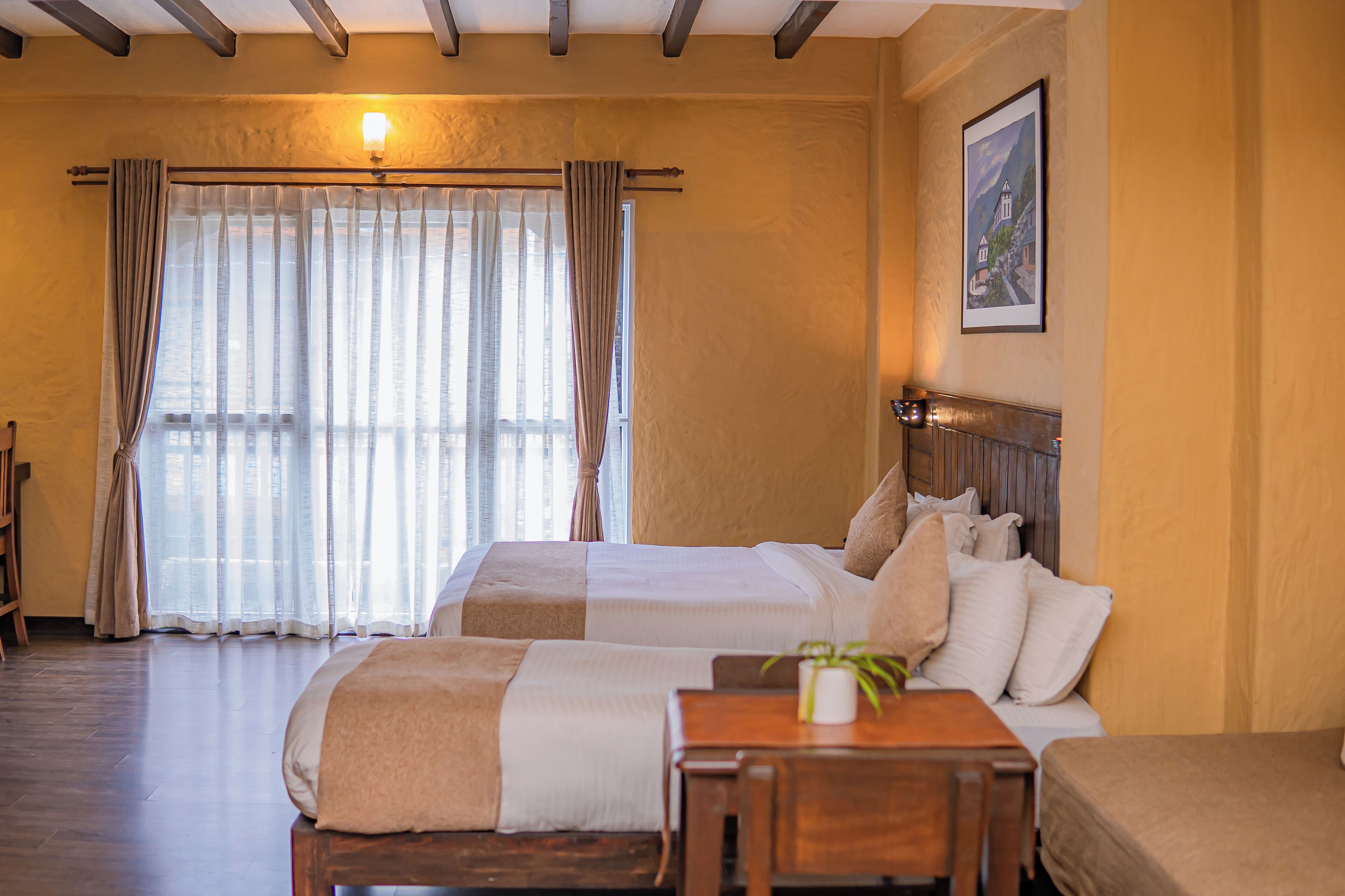 Ein Hotelzimmer mit zwei Betten, einem Holztisch und einem großen Fenster mit Vorhängen.