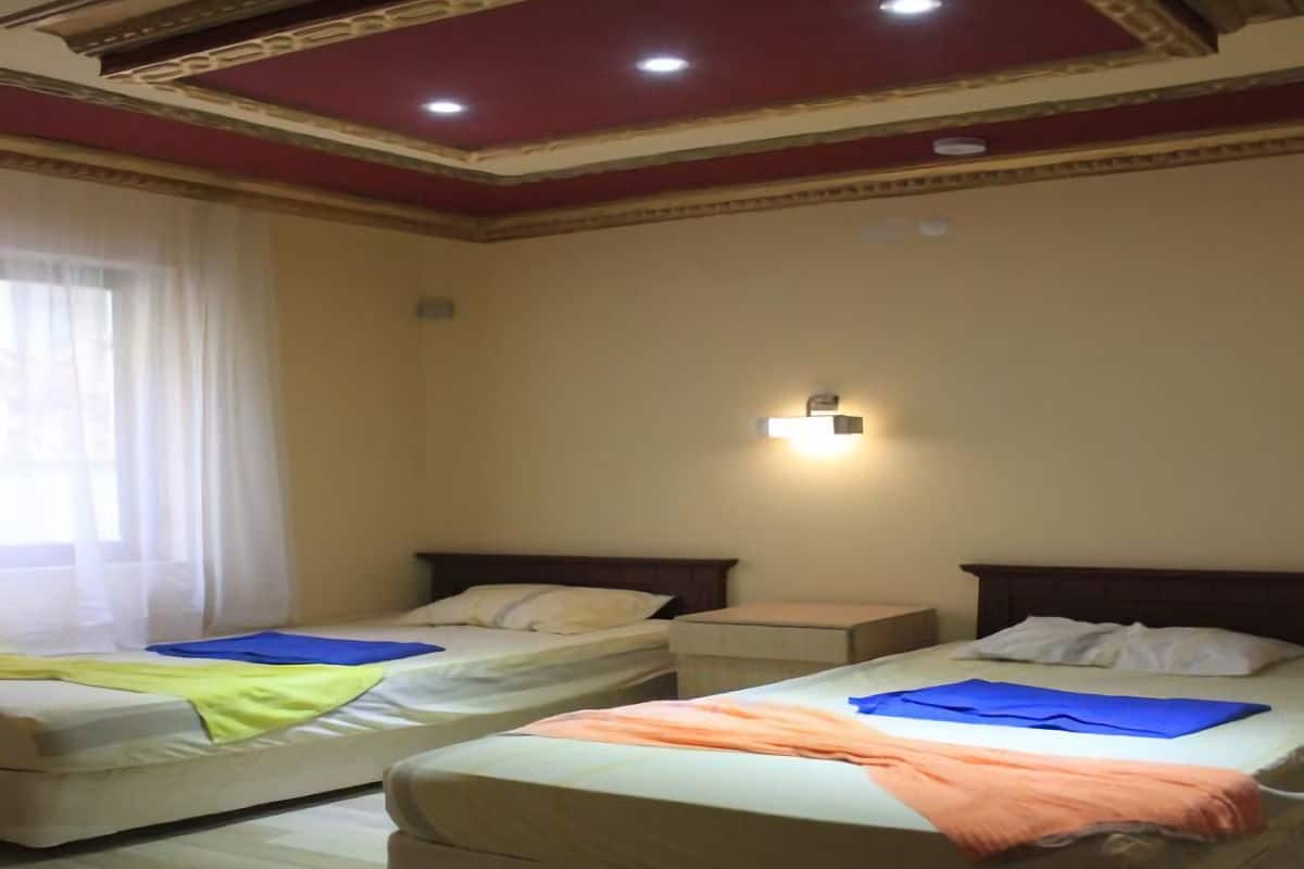 Une chambre d’hôtel avec deux lits simples, une table de chevet, une lampe fixée au mur et une fenêtre avec des rideaux.