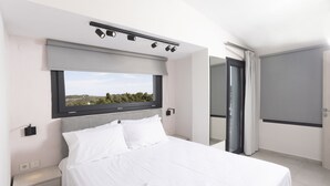 A modern hotel room with a large bed, a window with a view, a bedside table, and a door leading to a balcony. - Blue Avenue (Kassandra)