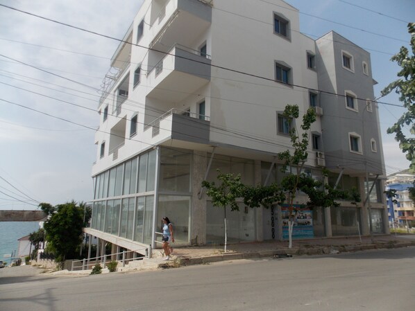 A multi-story building with a glass facade, a staircase leading to the entrance, and a view of the sea. - Doka Apartments 2 (Sarandë)