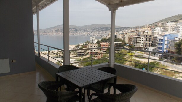 A balcony with a table and chairs, overlooking a coastal cityscape with buildings and hills. - Doka Apartments 2 (Sarandë)