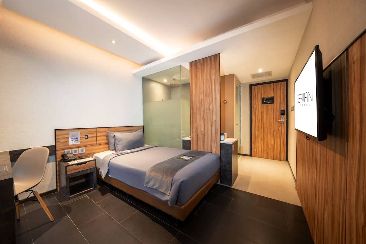 Una habitación de hotel moderna con cama, escritorio, silla, televisión y armario de madera.