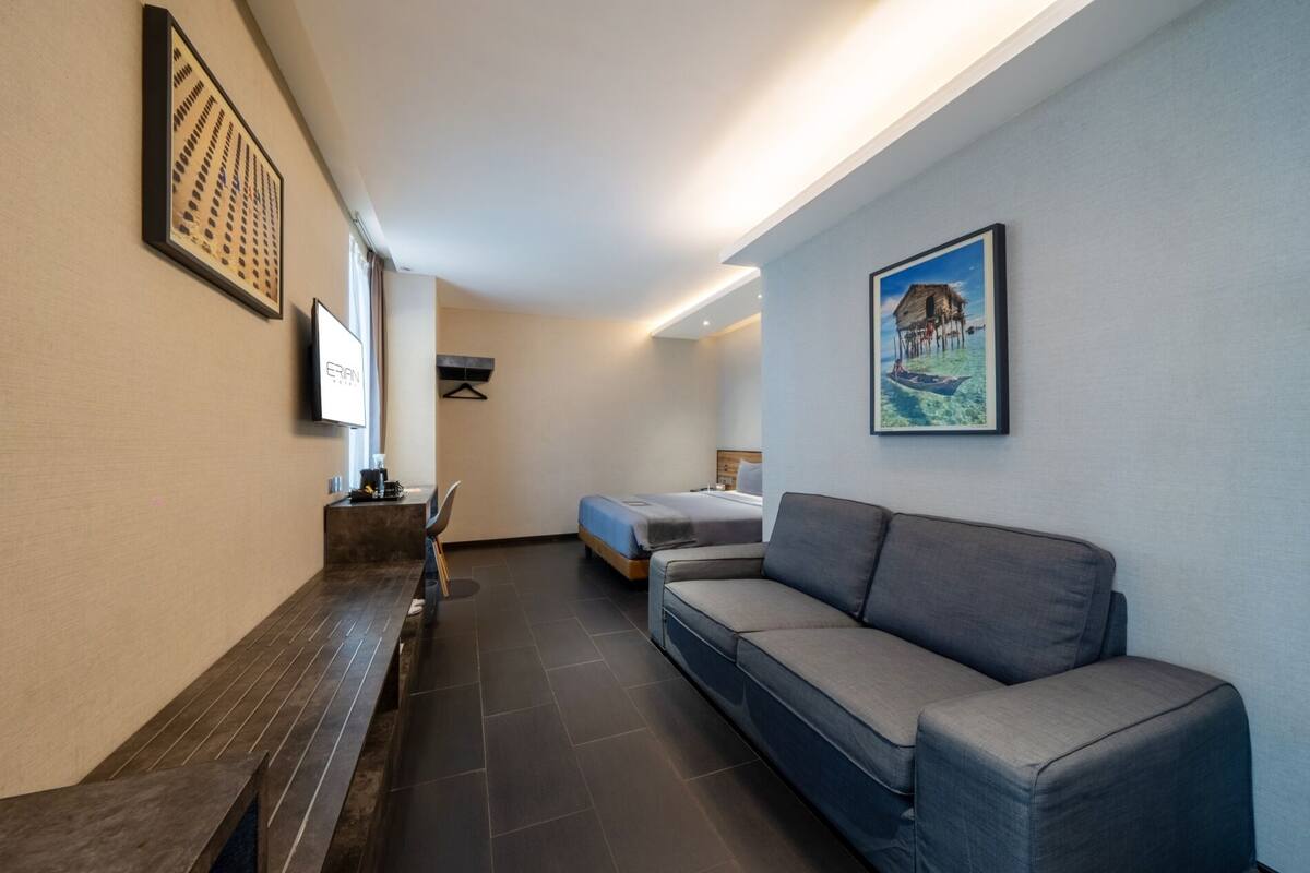 A modern hotel room with a sofa, a bed, a desk, and a TV.