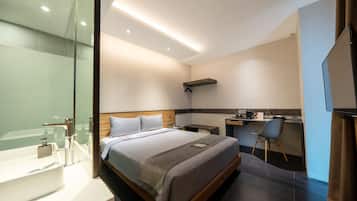 Una habitación de hotel moderna con una cama grande, un área de escritorio separada, un baño con cabina de ducha de vidrio y un televisor de pantalla plana.