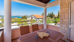 Un balcon avec une table en bois, deux chaises et une vue sur la mer et les montagnes.