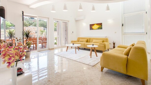 Un salon spacieux avec un canapé jaune, deux petites tables rondes et une grande fenêtre donnant sur un paysage verdoyant.