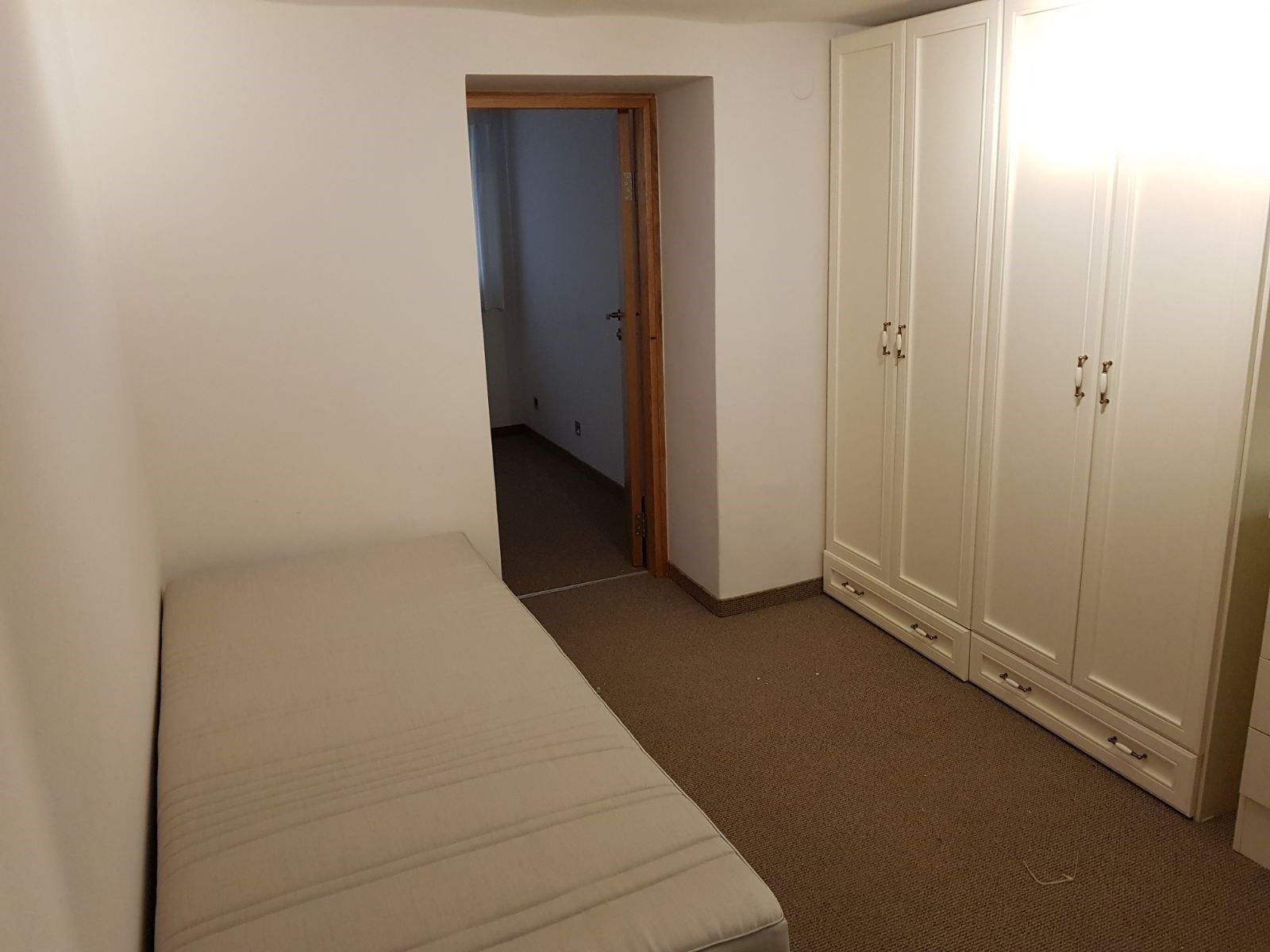 Une chambre avec un lit simple, une armoire et une porte donnant sur une autre pièce.