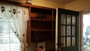 Ein Zimmer mit Holzstuhl, einem Tisch mit Blumenmuster-Tischdecke, einer grünen Tür und einem Fenster mit Vorhängen.