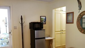 Ein kleines Zimmer mit einem Bett, einem Kühlschrank, einer Bank und einer Tür zu einer Küchenzeile.